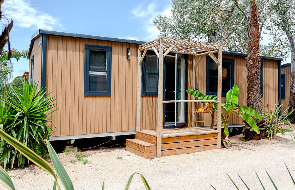 Mobil-home en bois avec terrasse, palmiers autour.
