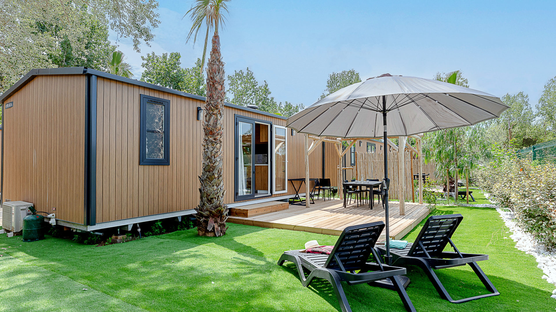 Terrasse avec parasol et chaises longues devant mobil-home.