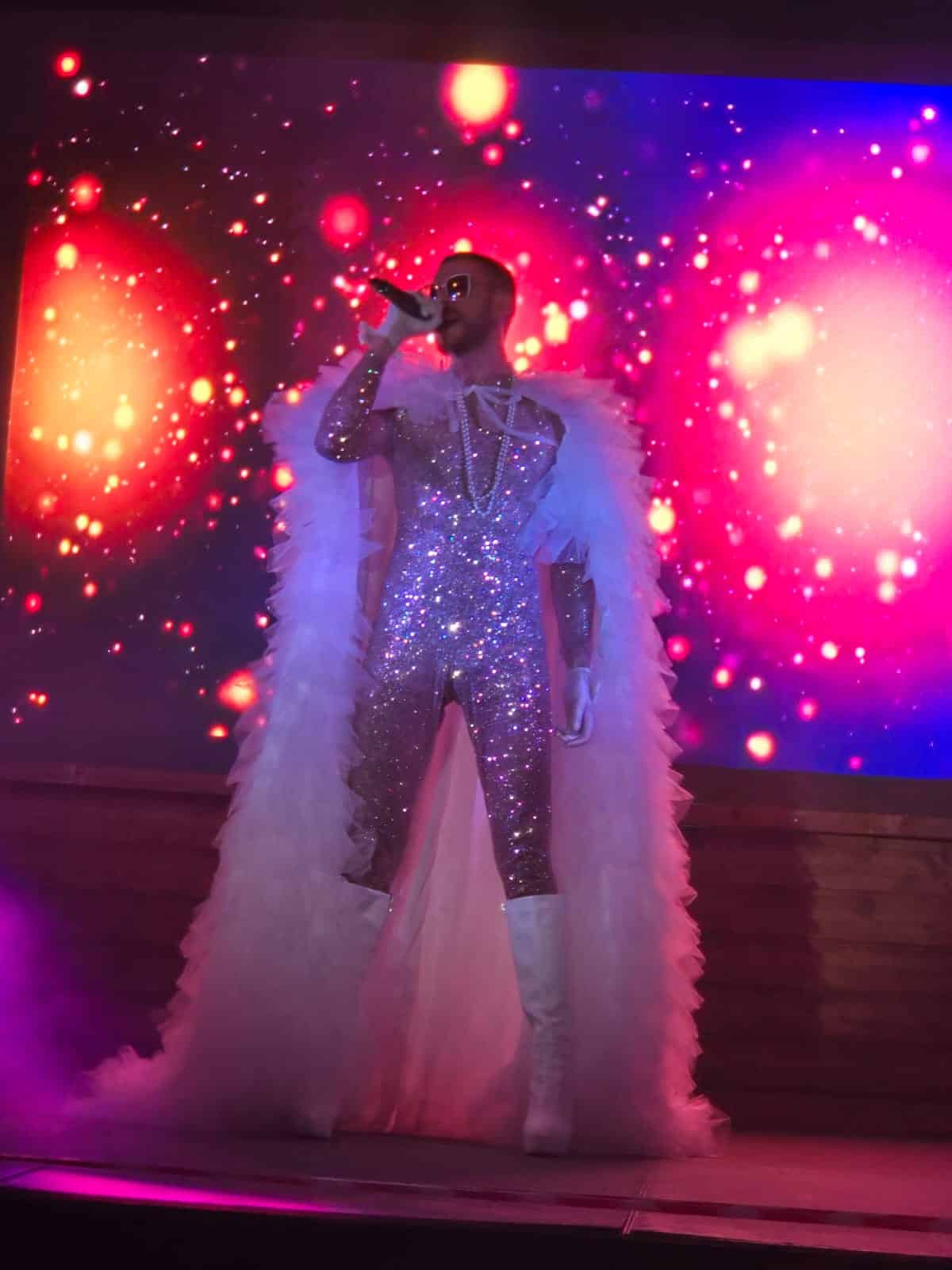 Sänger in einem glitzernden Anzug auf einer bunten Bühne.