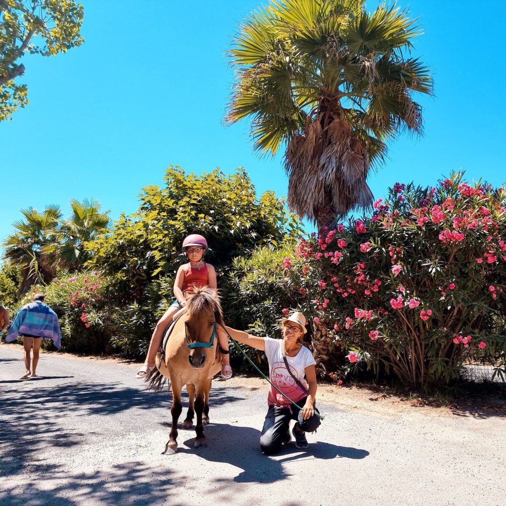 Enfant à poney, adulte à côté, journée ensoleillée.