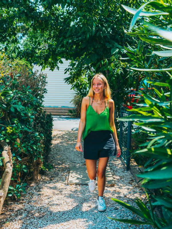 Femme souriante marchant dans un jardin ensoleillé.