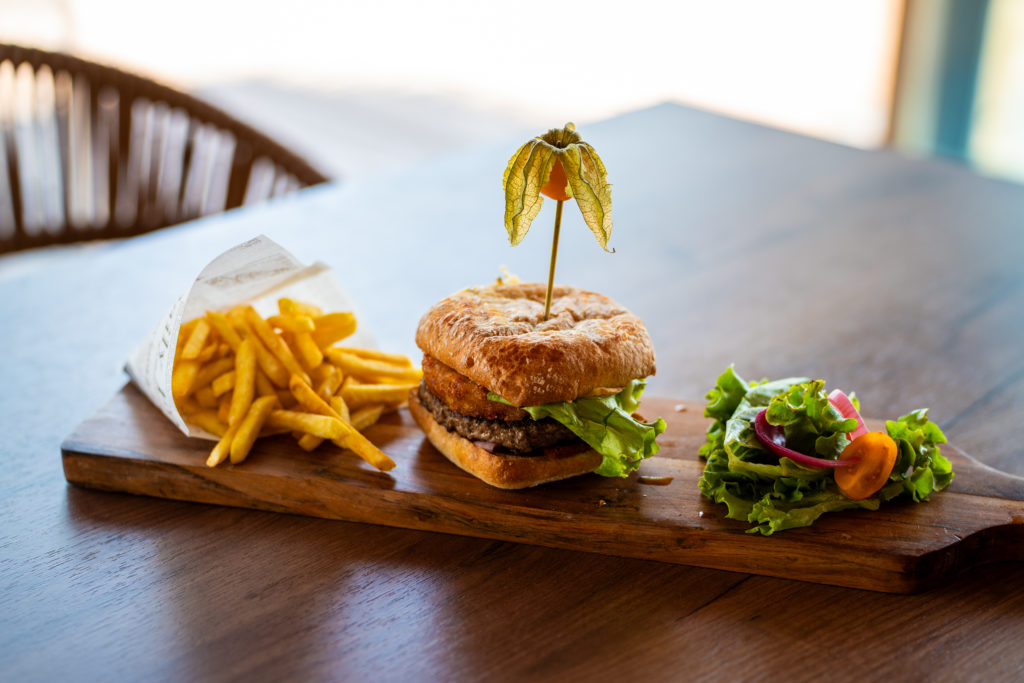Burger, frites et salade sur planche en bois.