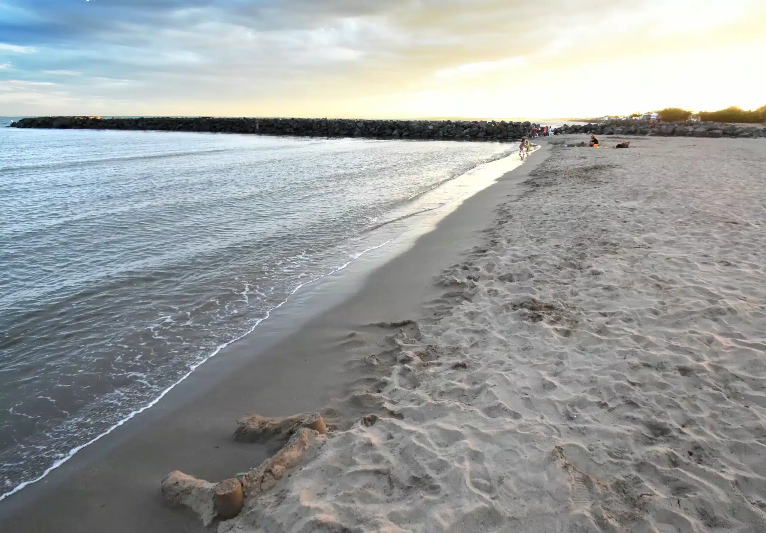 Plage au coucher du soleil, ciel nuageux.