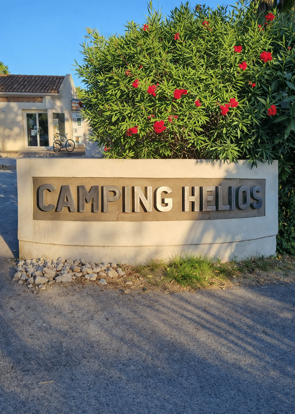 Entrée du Camping Helios avec arbustes fleuris.