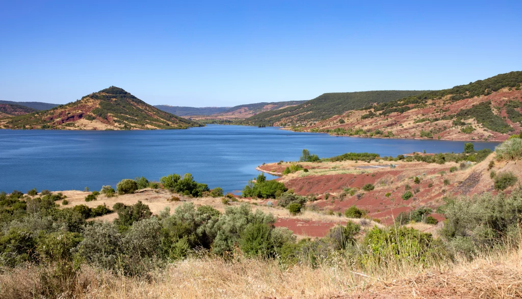 Lac entouré de collines verdoyantes sous ciel bleu.