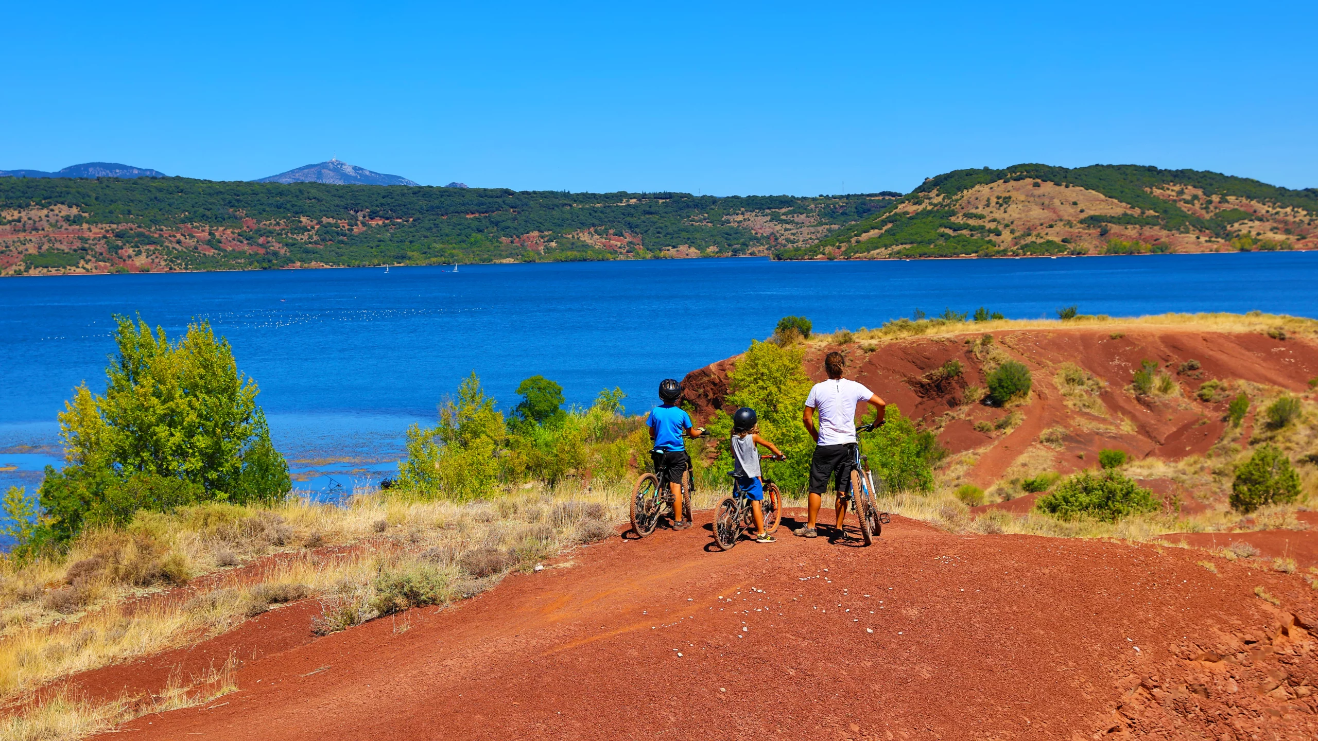Cyclistes devant lac et collines verdoyantes.