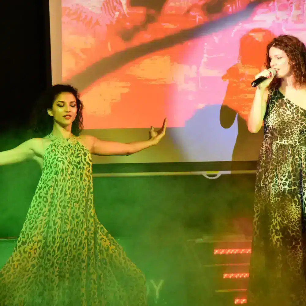 Deux femmes chantent sur scène en robes imprimées.