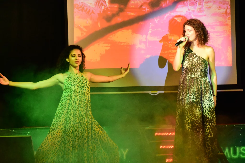 Deux femmes chantent sur scène en robes imprimées.