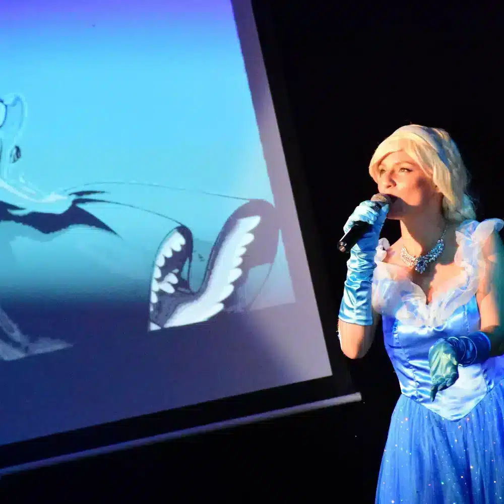 Femme chantant déguisée en princesse devant écran.