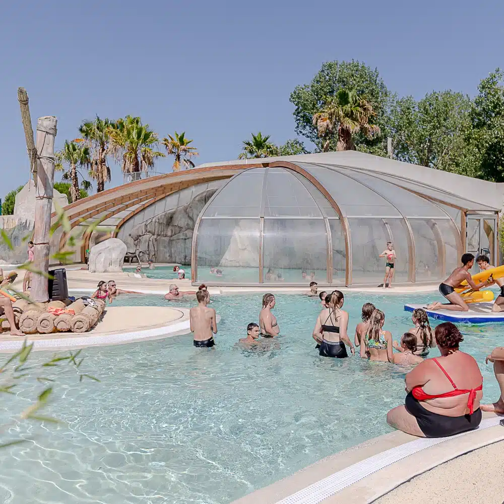 Piscine extérieure animée avec des baigneurs et palmiers.