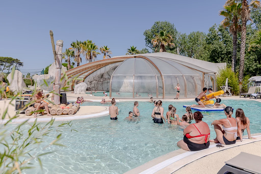 Piscine extérieure animée avec des baigneurs et palmiers.