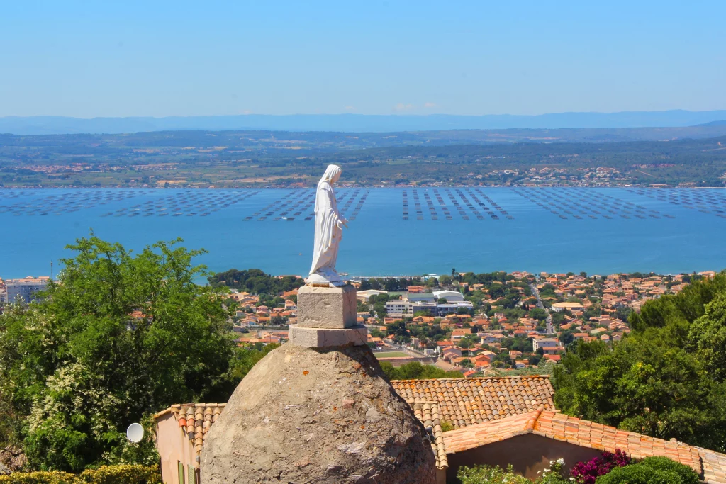 Statue surplombant une ville méditerranéenne et la mer.