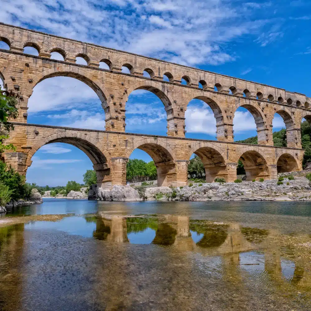 Pont antique en pierres sur rivière, ciel bleu.