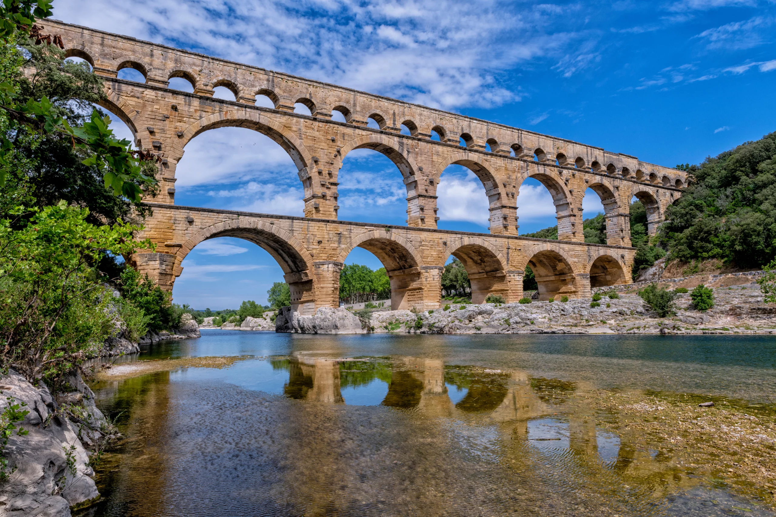 Pont antique en pierres sur rivière, ciel bleu.